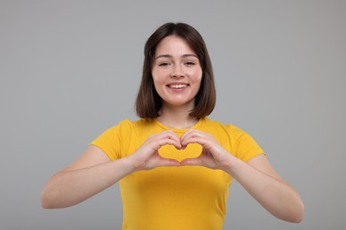 Photo of Happy woman showing heart gesture with hands on grey background
