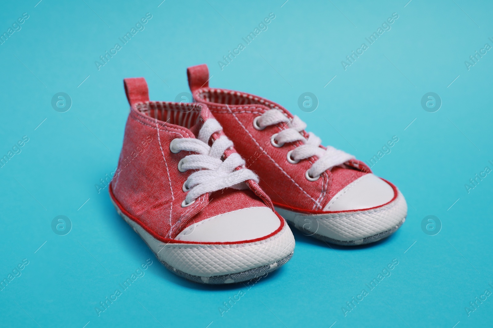 Photo of Pair of cute baby shoes on light blue background