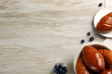 Delicious baked pirozhki and blueberries on wooden table, flat lay. Space for text
