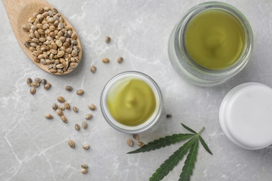 Jars of hemp cream and seeds on grey table, flat lay. Organic cosmetics