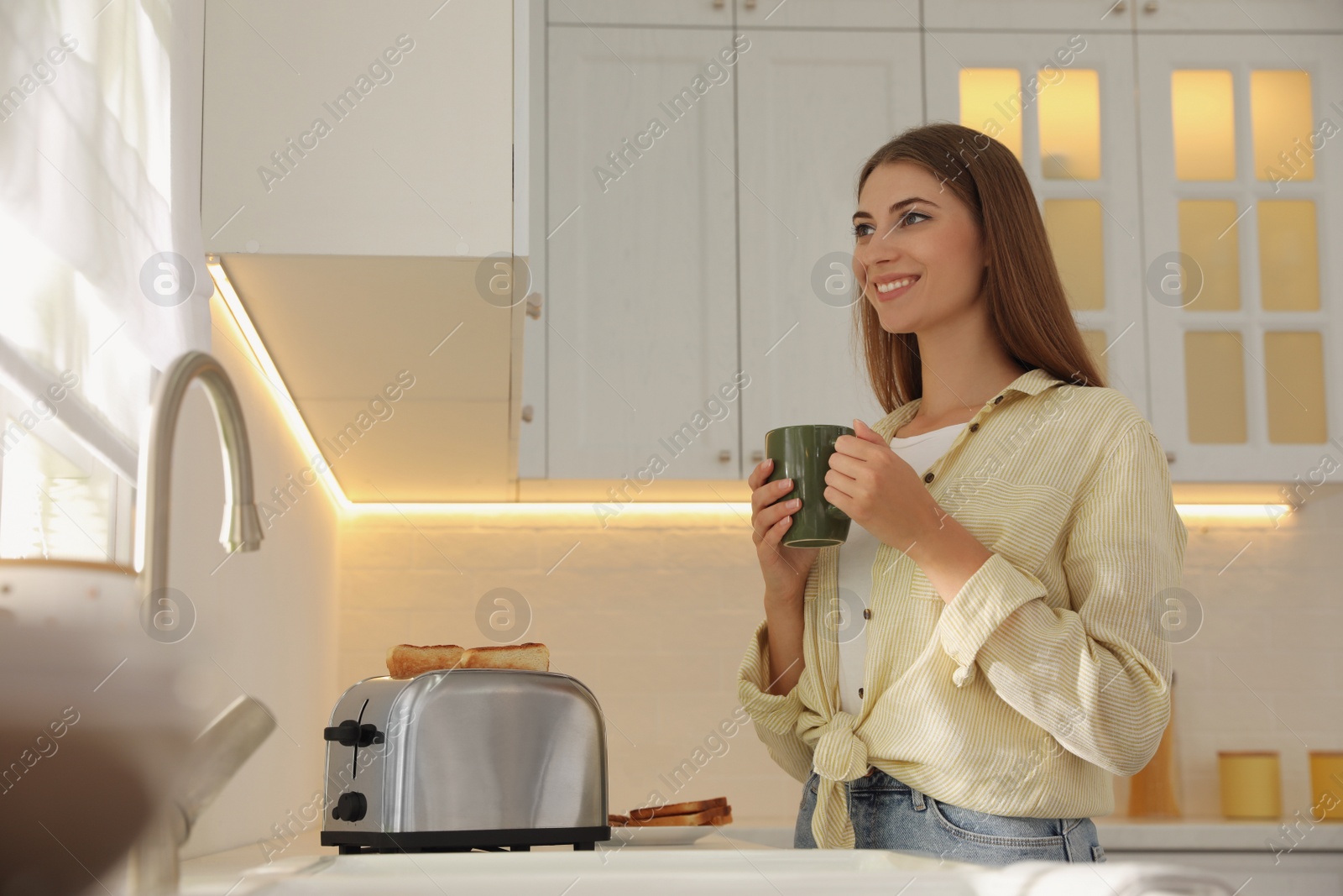 Photo of Young woman near toaster with slices of bread in kitchen