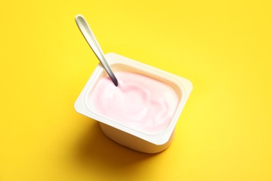 Plastic cup with creamy yogurt and spoon on color background