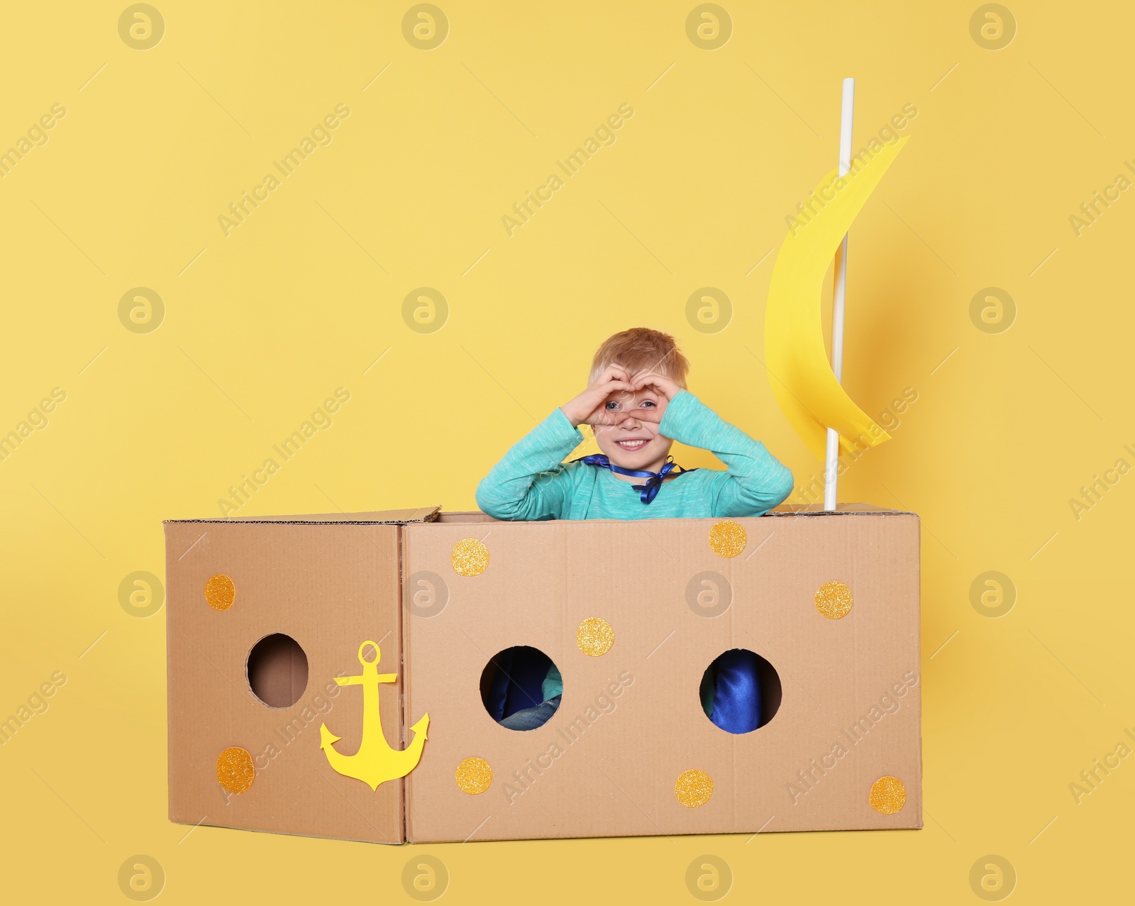 Photo of Little child playing with ship made of cardboard box on yellow background