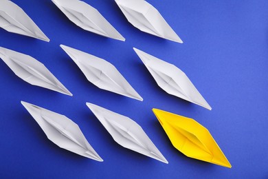 Yellow paper boat leading others on blue background, flat lay. Leadership concept