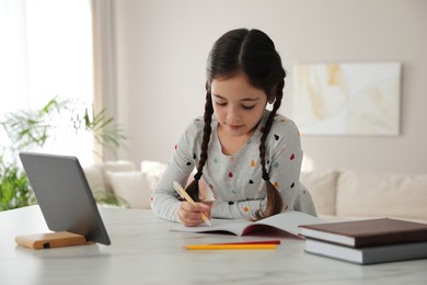 Little girl doing homework with modern tablet at home