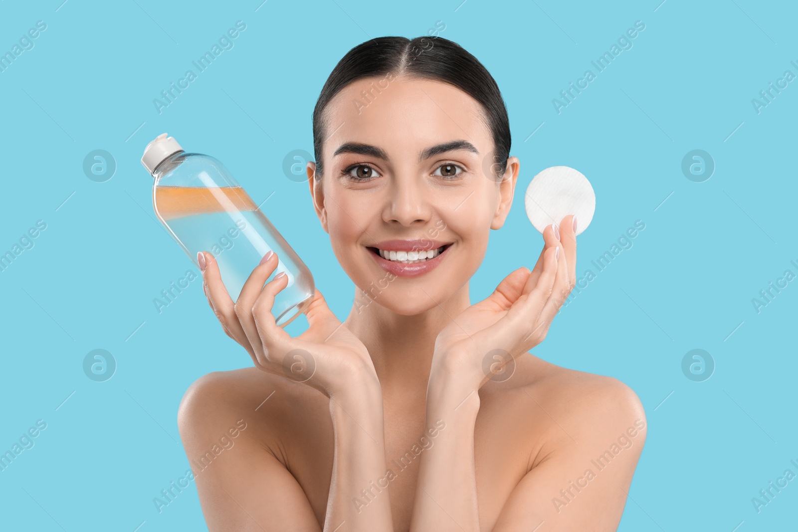 Photo of Beautiful woman holding makeup remover and cotton pad on light blue background