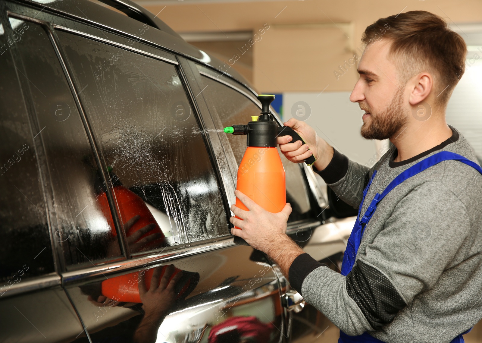 Photo of Skilled worker washing tinted car window in shop