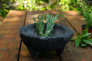 Mortar with thyme and rosemary on wooden table outdoors. Aromatic herbs