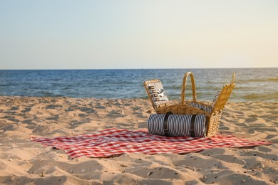 Blanket with picnic basket on sandy beach near sea, space for text