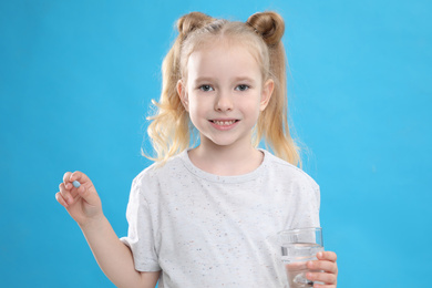 Little girl with vitamin pill and glass of water on blue background