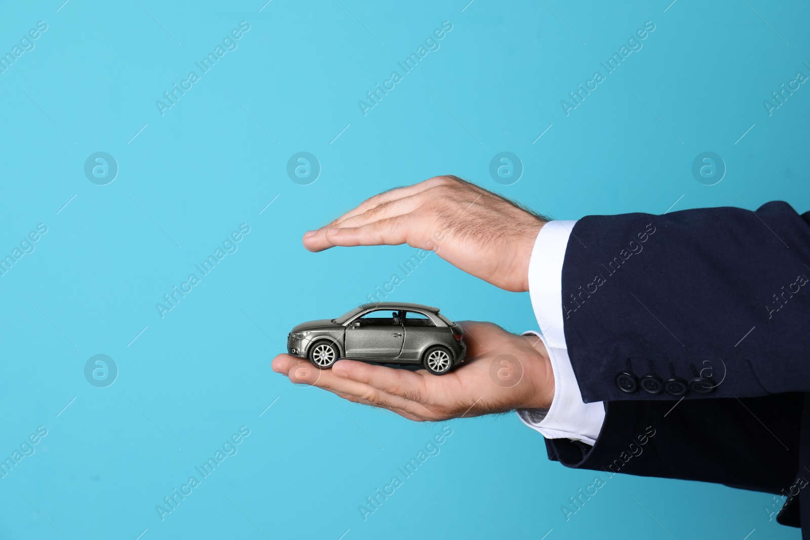 Photo of Male insurance agent holding toy car on color background, closeup. Space for text