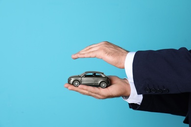 Photo of Male insurance agent holding toy car on color background, closeup. Space for text