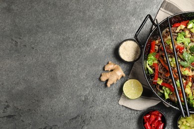 Photo of Wok with noodles, mushrooms, vegetables and other products on grey table, flat lay. Space for text