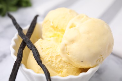 Photo of Delicious ice cream and vanilla pods on white table, closeup