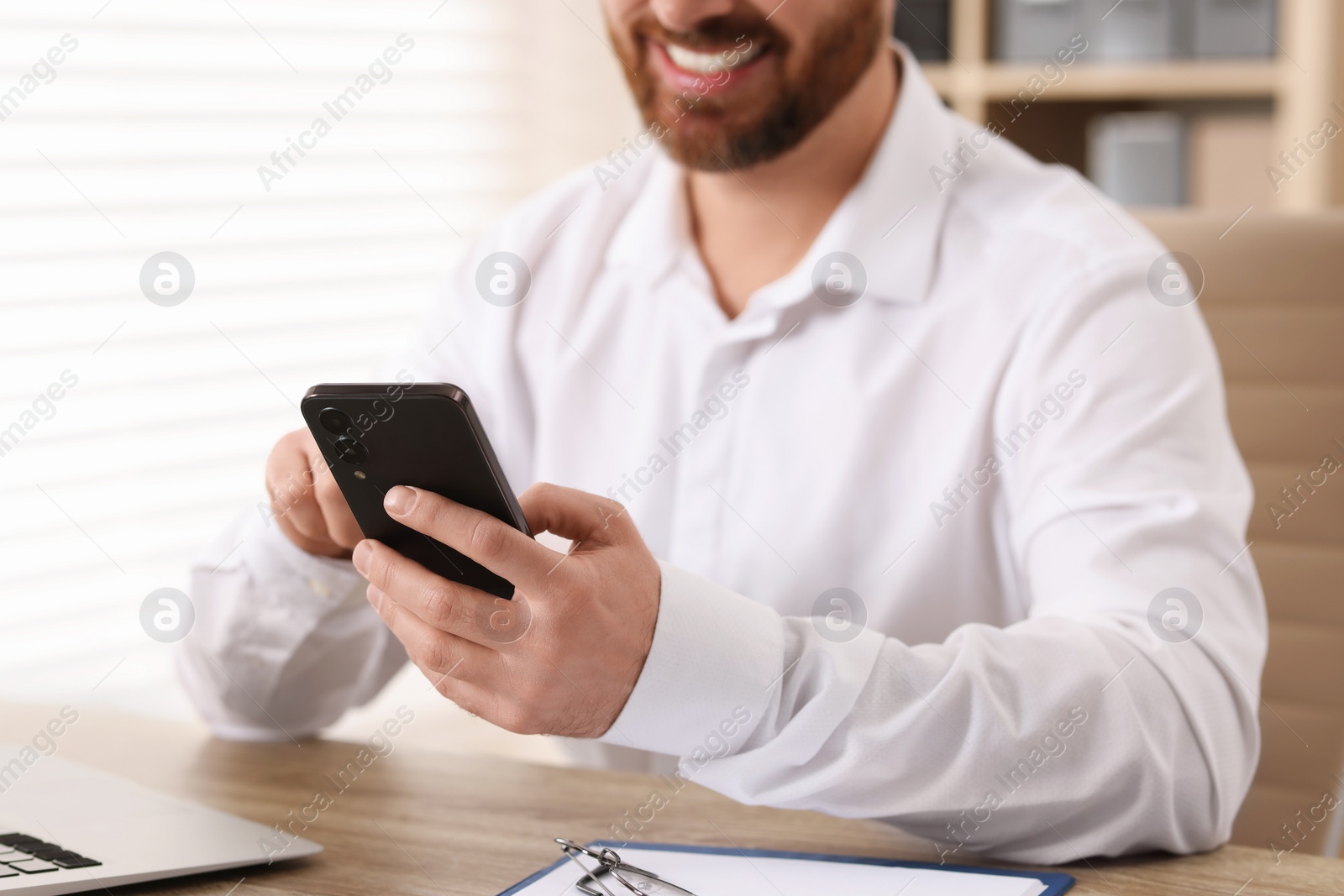 Photo of Smiling man using smartphone at table in office, closeup