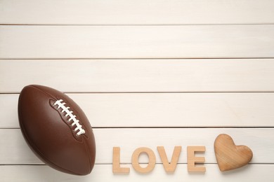 Photo of American football ball, heart and word Love on white wooden background, flat lay. Space for text
