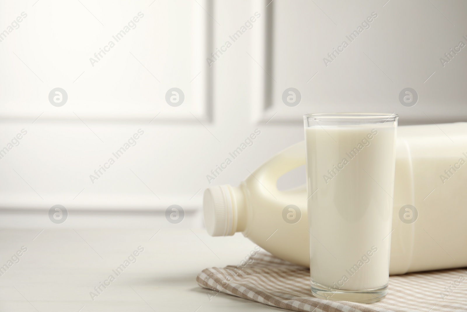 Photo of Gallon bottle and glass of milk on white wooden table. Space for text