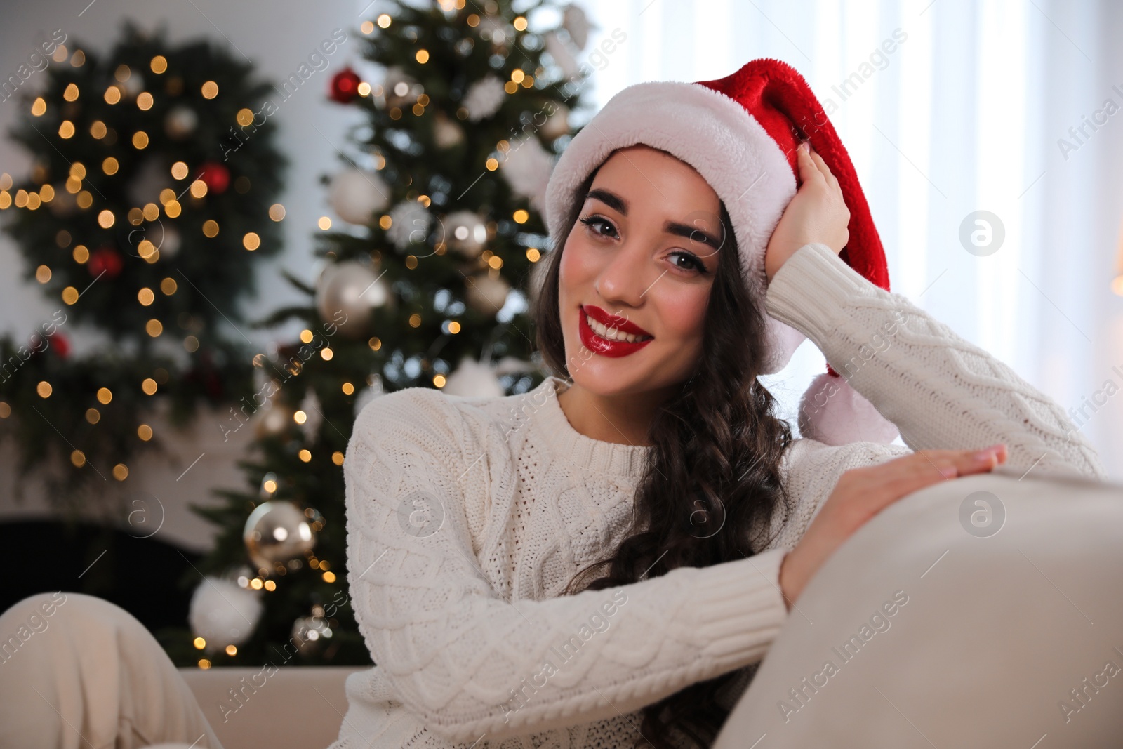 Photo of Beautiful young woman wearing Santa hat in room decorated for Christmas