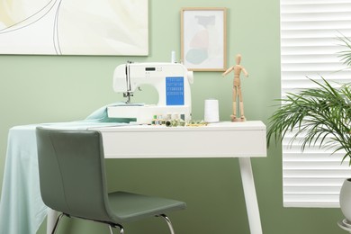 Photo of Modern sewing machine with cloth and craft accessories on white table near window in room