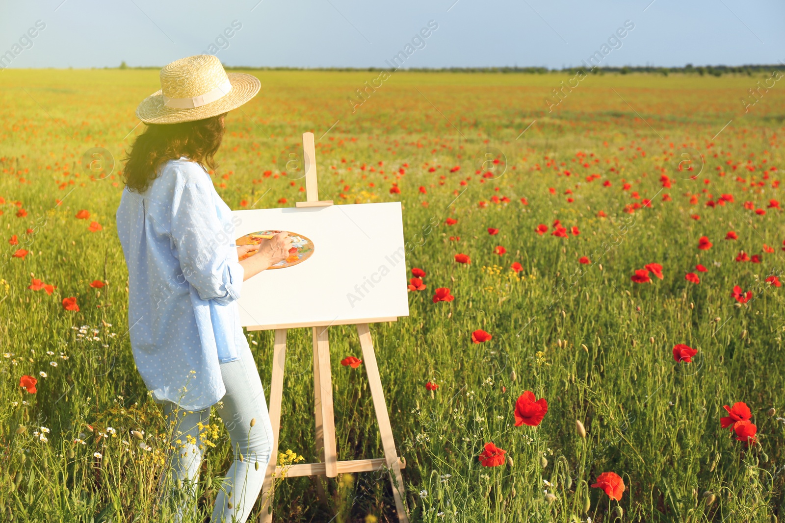 Photo of Woman painting on easel in beautiful poppy field