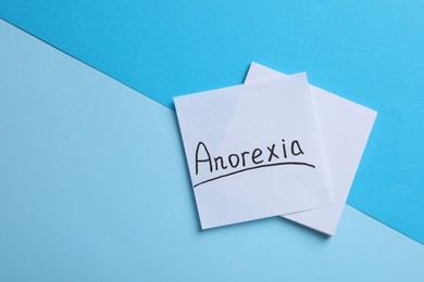 Note papers with word Anorexia on light blue background, flat lay. Space for text