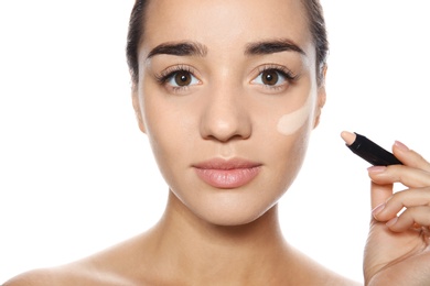 Young woman applying foundation on her face against white background