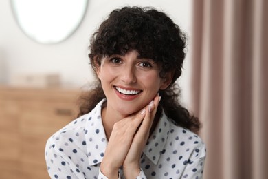 Portrait of beautiful woman with curly hair indoors. Attractive lady smiling and looking into camera