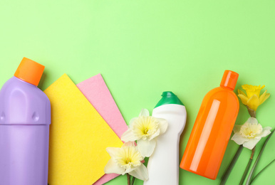 Photo of Composition with spring flowers and cleaning supplies on light green background, flat lay. Space for text