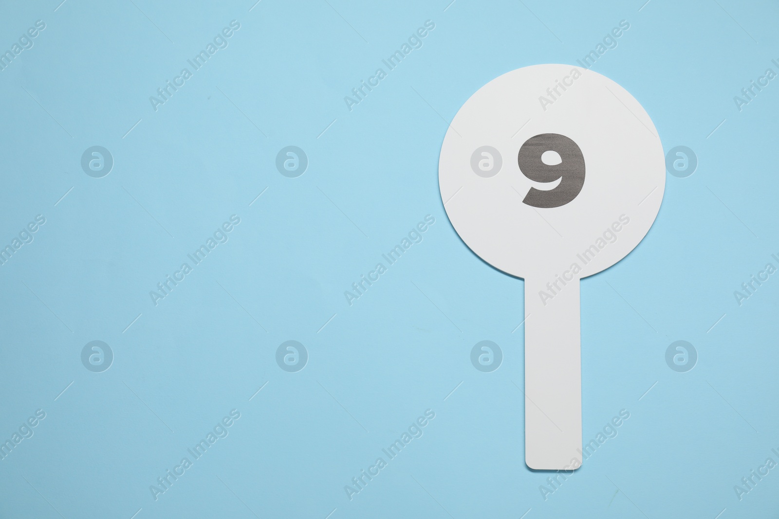 Photo of Auction paddle with number 9 on light blue background, top view. Space for text
