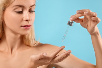 Beautiful woman applying cosmetic serum onto her hand on light blue background