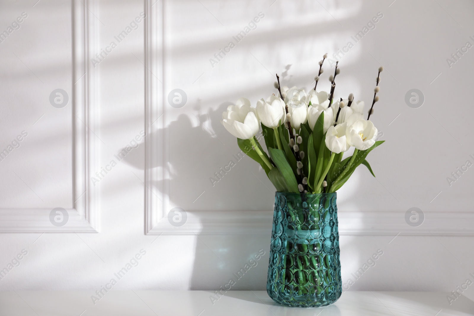 Photo of Beautiful bouquet of willow branches and tulips in vase near white wall, space for text