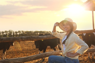Photo of Young woman standing near cow pen on farm. Animal husbandry