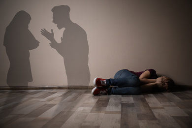Little girl closing her eyes on floor indoors and silhouettes of arguing parents 