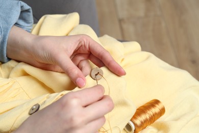 Photo of Woman sewing button with needle and thread onto shirt at home, closeup