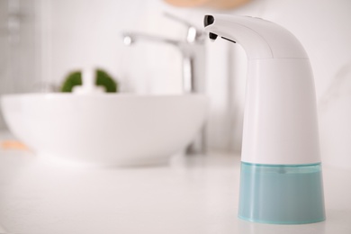 Photo of Modern automatic soap dispenser on countertop in bathroom. Space for text