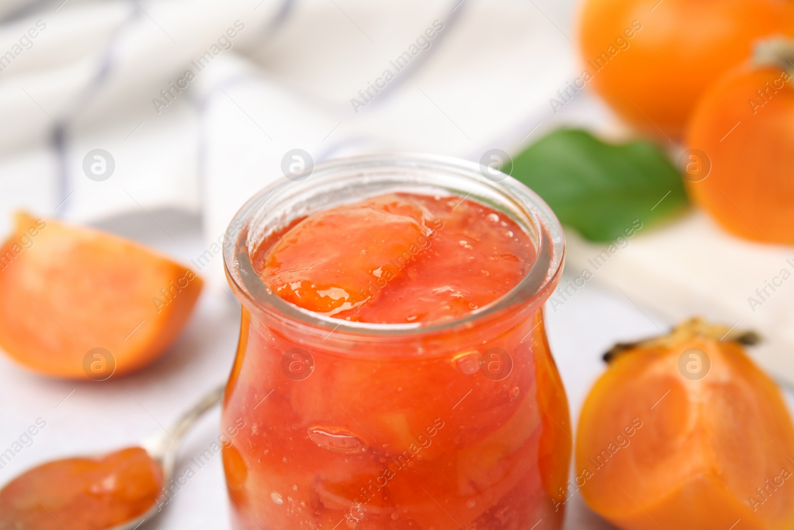 Photo of Jar of tasty persimmon jam on white table, closeup