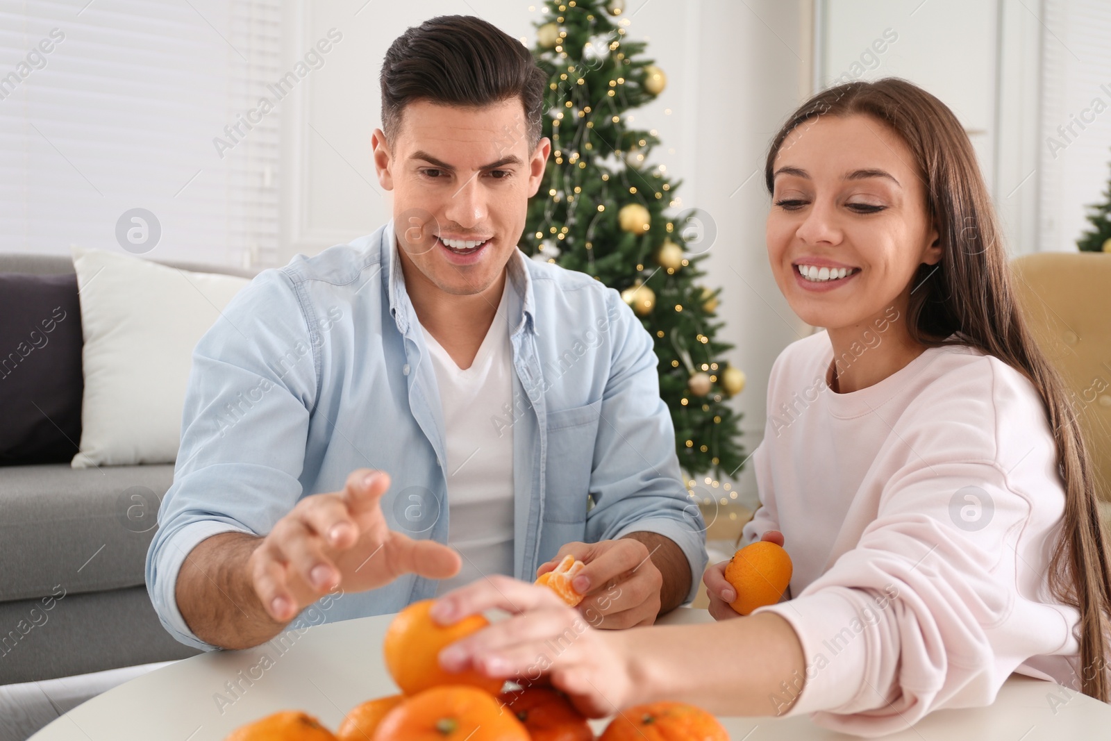 Photo of Happy couple with tangerines in room decorated for Christmas