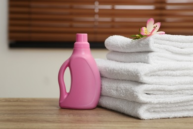 Photo of Stack of clean towels with flower and detergent on table indoors. Space for text