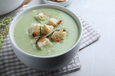 Photo of Bowl of delicious asparagus soup served on light grey table