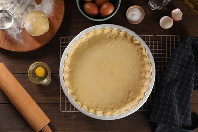 Photo of Pie tin with fresh dough, rolling pin and ingredients on wooden table, flat lay. Making quiche