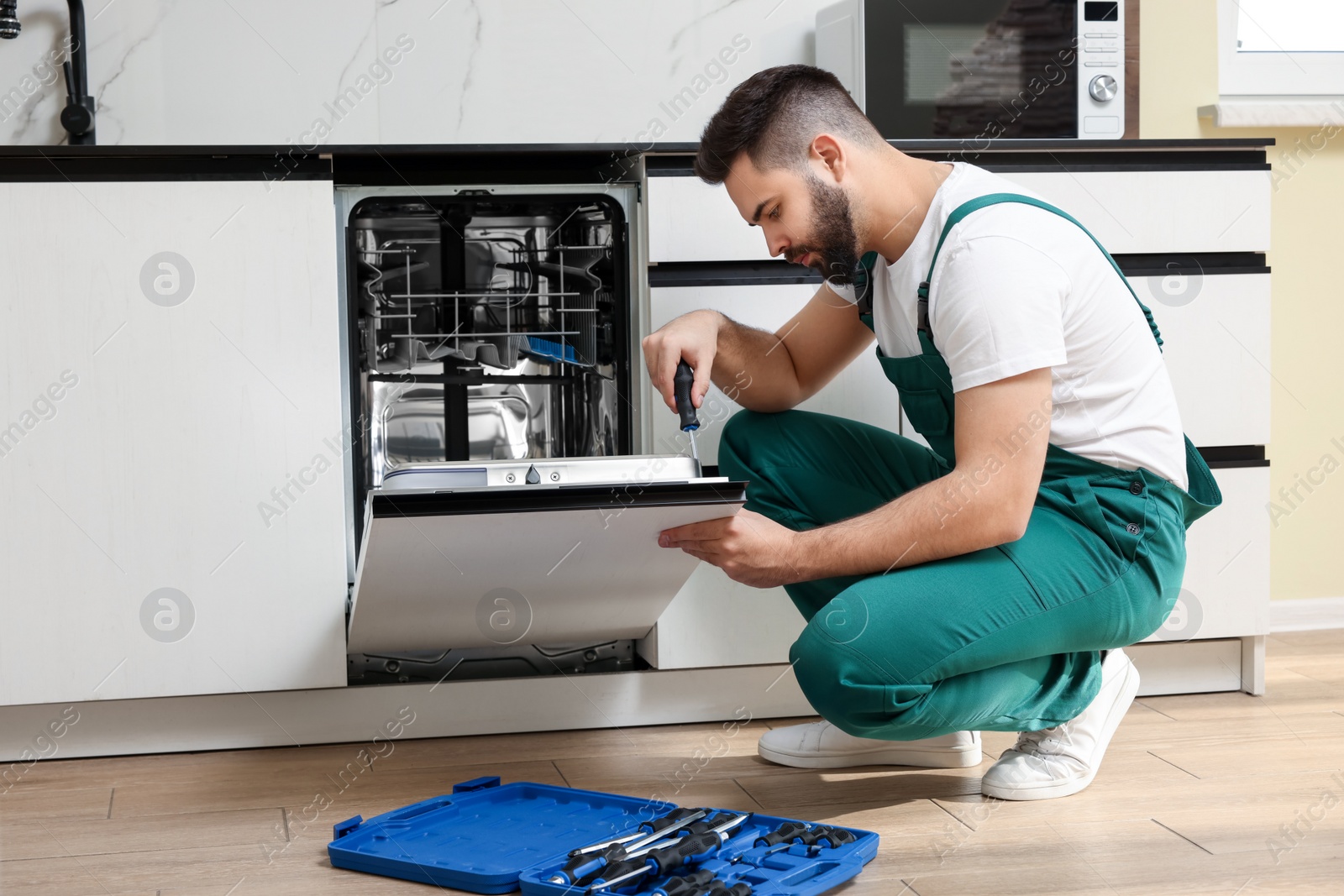 Photo of Serviceman repairing dishwasher door with screwdriver in kitchen