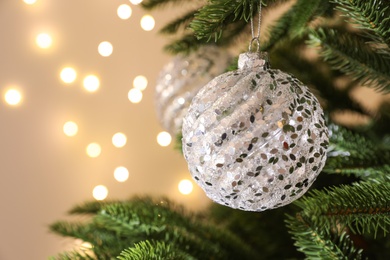 Photo of Beautiful holiday bauble hanging on Christmas tree against blurred lights, closeup. Space for text