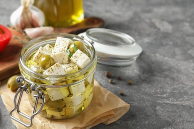 Composition with pickled feta cheese in jar on grey table, space for text