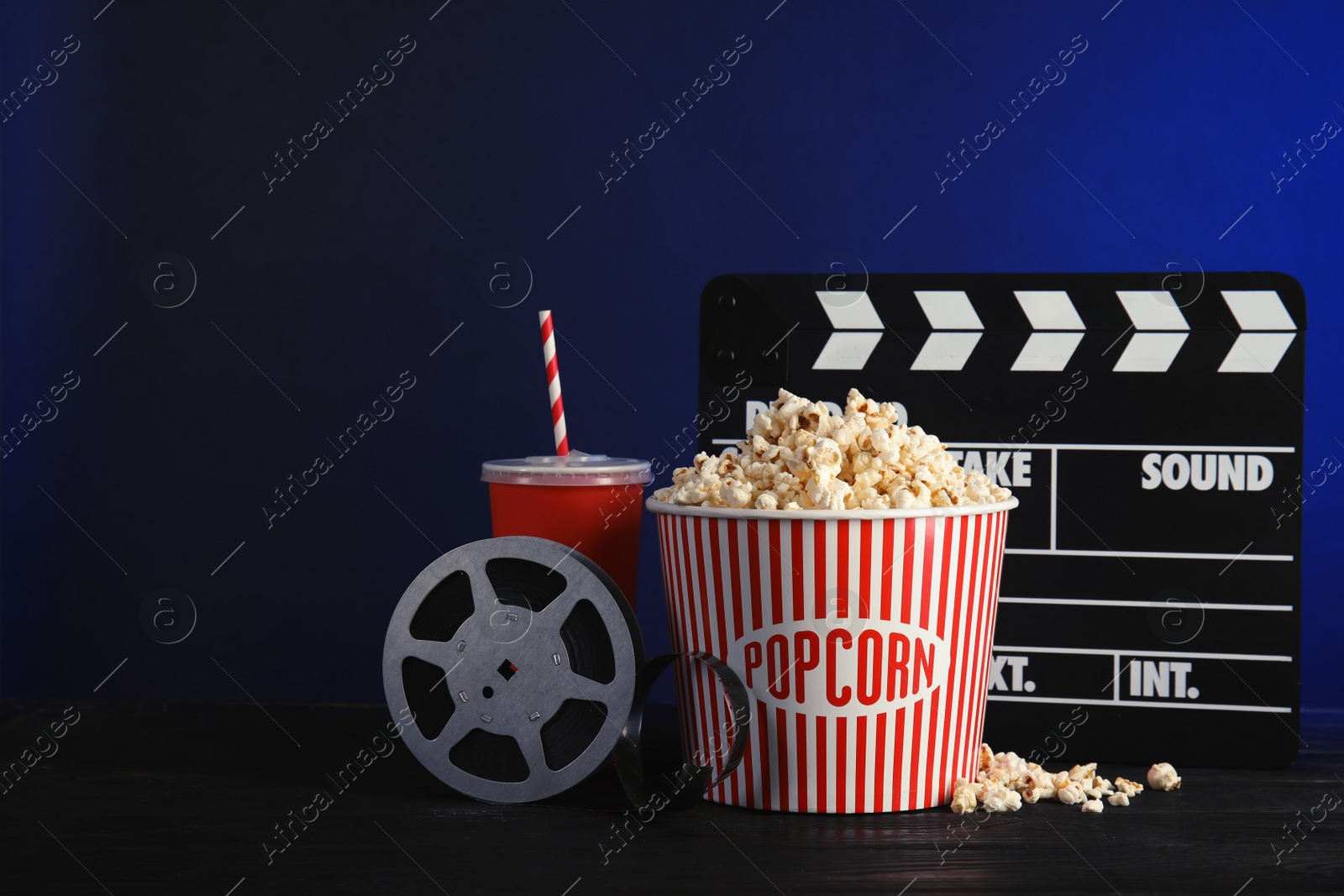 Photo of Composition with popcorn, cinema clapperboard and film reel on table against color background. Space for text