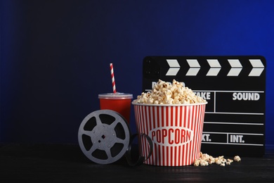 Composition with popcorn, cinema clapperboard and film reel on table against color background. Space for text