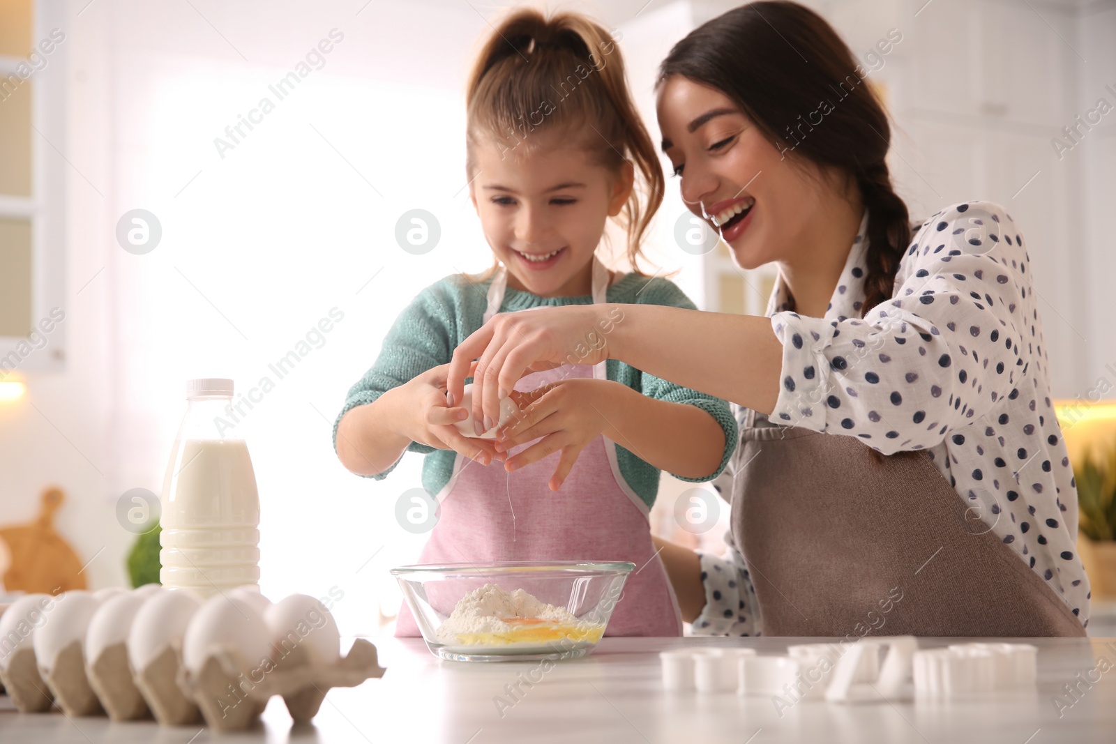 Photo of Mother and daughter making dough at table in kitchen