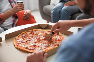 Photo of Man cutting fresh pizza on table, closeup