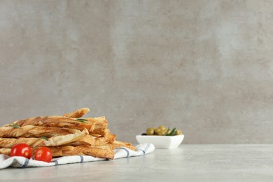 Photo of Fresh delicious grissini with rosemary and tomatoes on light grey table, space for text