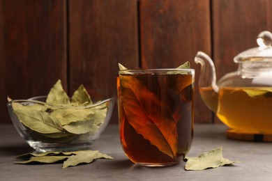 Cup of freshly brewed tea with bay leaves on grey table