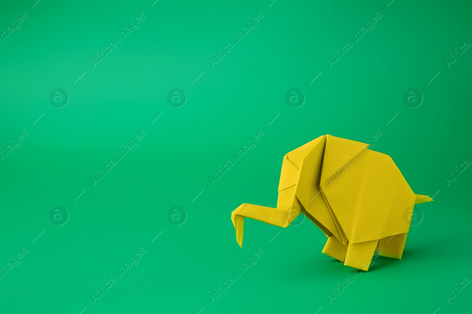 Photo of Origami art. Paper elephant on green background, space for text